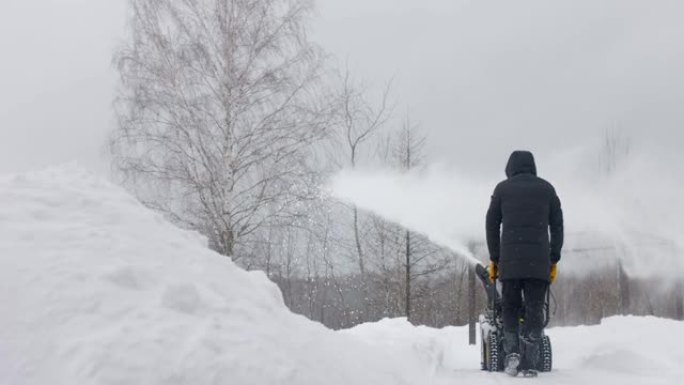 男子在院子里用机械扫雪机除雪。后视图。慢动作