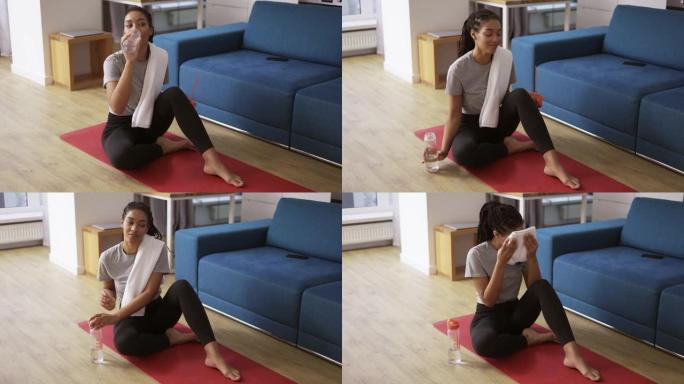 运动的非洲裔美国妇女在家在瑜伽垫上锻炼后喝水