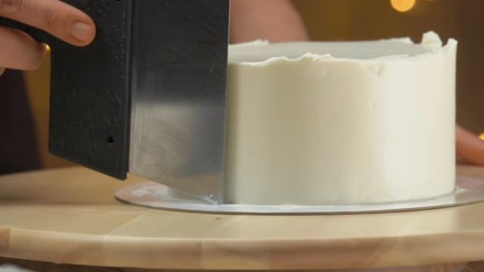 糕点厨师的特写镜头用刮刀将蛋糕上的奶油抹平