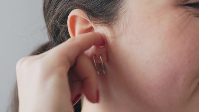 一个用手指用耳环在耳朵里抓挠的女人的脸部特写。耳痛和耳聋的概念