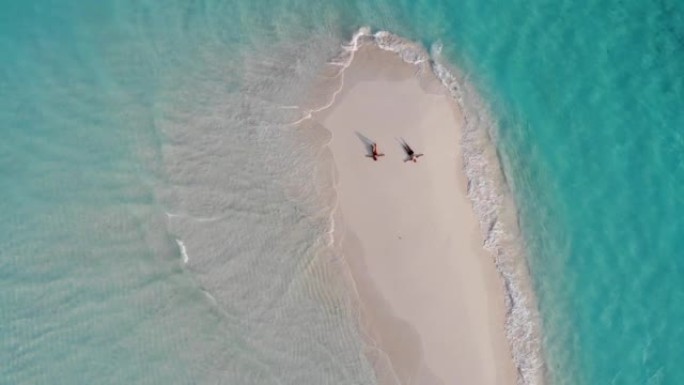白种人夫妇躺在沙洲上的无人机鸟瞰图，手臂散布在绿松石水，白沙和小浪之间，达拉万德胡，马尔代夫，印度洋