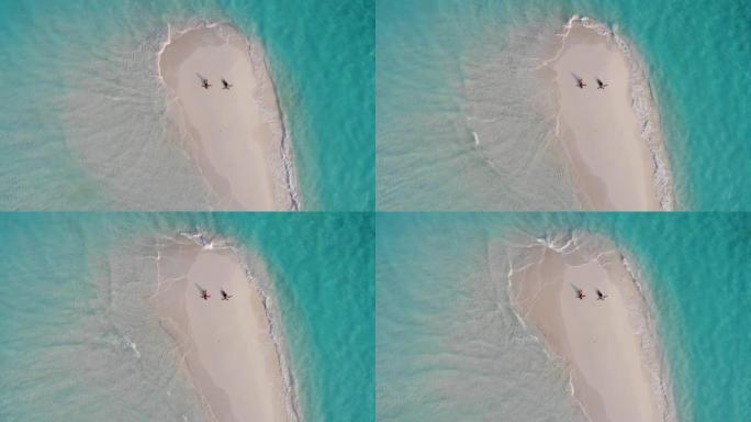 白种人夫妇躺在沙洲上的无人机鸟瞰图，手臂散布在绿松石水，白沙和小浪之间，达拉万德胡，马尔代夫，印度洋