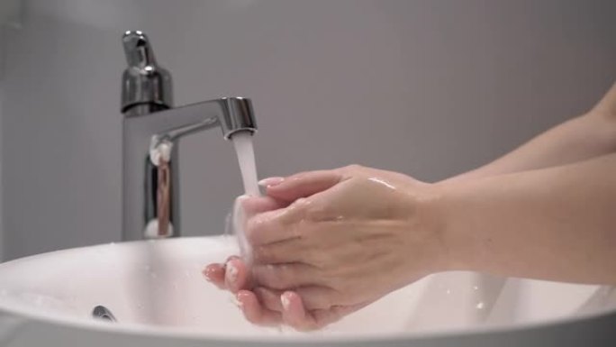 女人洗手。女性用水打开水龙头，双手在水槽中冲洗