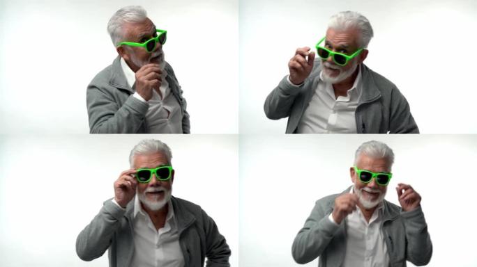 时尚的情感老人养老金领取者，戴着绿色眼镜的灰色胡须，在白色孤立的背景上与有趣的情感共舞。开朗有趣无忧