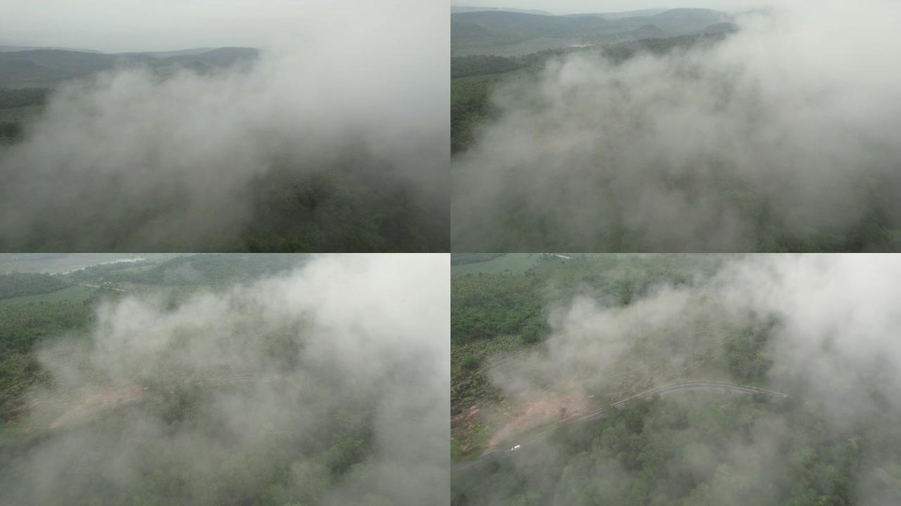 空中无人机电影拍摄的汽车和道路在早上下雨后越过山顶，有雾和绿色森林。