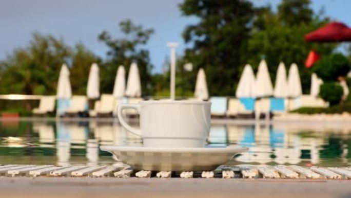 在夏季晴天，在游泳池的背景上特写一杯白咖啡或热饮。早上好概念，并计划新的一天，一周，一个月。度假和旅