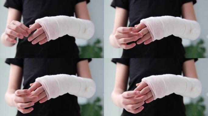 用白色石膏绷带包裹的断手手指做按摩的孩子。医疗保健概念。女孩在黑色t恤的背景下折断了手臂