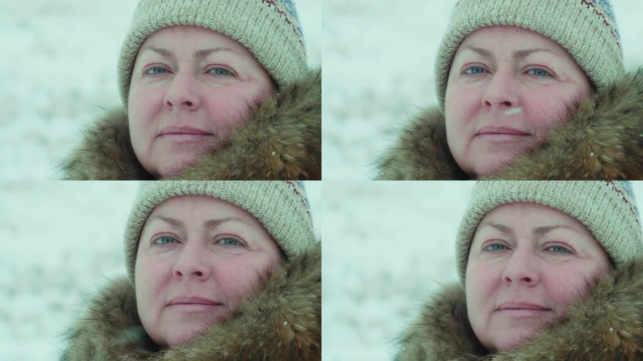 一位45岁的女人在降雪下戴着帽子和皮草项圈微笑的慢动作肖像。冬季景观