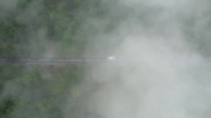 空中无人机电影拍摄的汽车和道路在早上下雨后越过山顶，有雾和绿色森林。