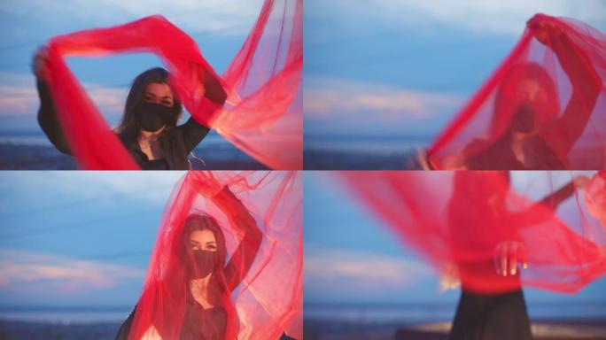 戴面具的女孩在屋顶用红色透明织物摆姿势
