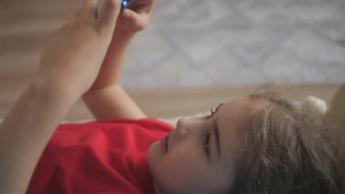 孩子躺在沙发上在家打电话玩游戏。在手机上玩电子游戏的女孩。青少年在沙发上玩电子游戏智能手机。孩子使用