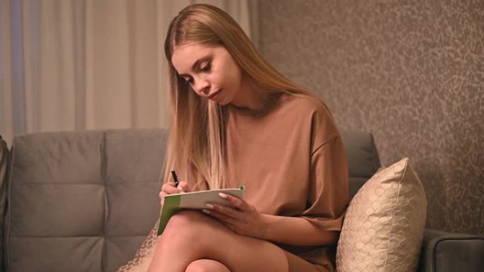 一个十几岁的女孩正在用笔记本电脑在家上学，在笔记本上做笔记。关于沙发、远程学习和工作的研究