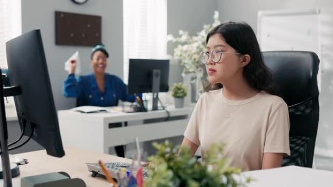 上班族坐在电脑前的办公桌前，在韩国美女的女人周围闲逛。另一个女孩因向同事扔纸飞机而感到不安