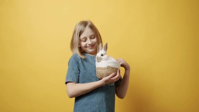 穿着蓝色连衣裙的少年拿着一个篮子，手里拿着一只兔子