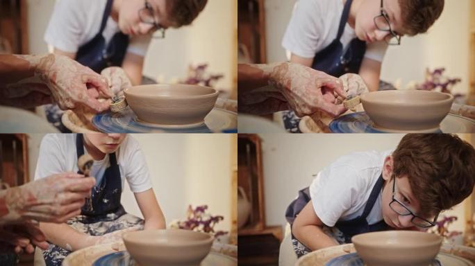 一个年轻的少年男孩坐在陶工的轮子上，在老师的帮助下，用特殊的工具在陶土上画了一幅画