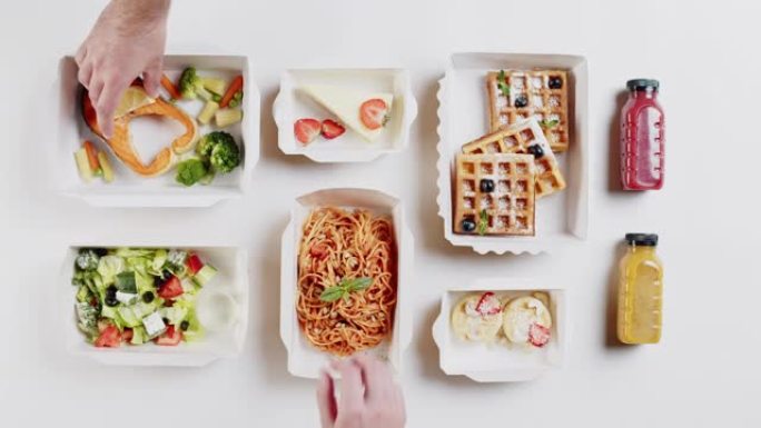 送餐俯视图，在白色背景上的一次性容器中带走餐点。午餐盒特写，里面有熟鱼、沙拉、意大利面和比利时华夫饼