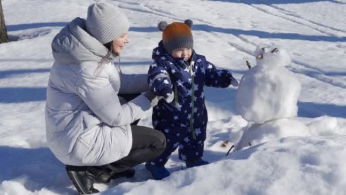 孩子在雪地里迈出了第一步，和妈妈一起散步。1岁的男婴在冬天学习与妈妈在公园散步。