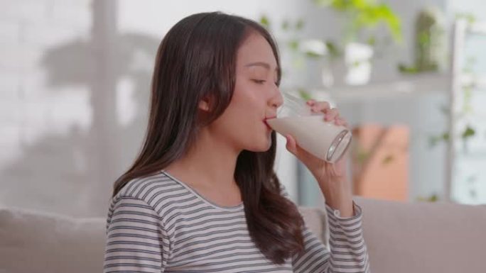 健康年轻的亚洲女性在家中喝钙牛奶，强壮的骨骼，微笑的印度女性在玻璃上拿着豆浆享受营养健康生活，天然牛