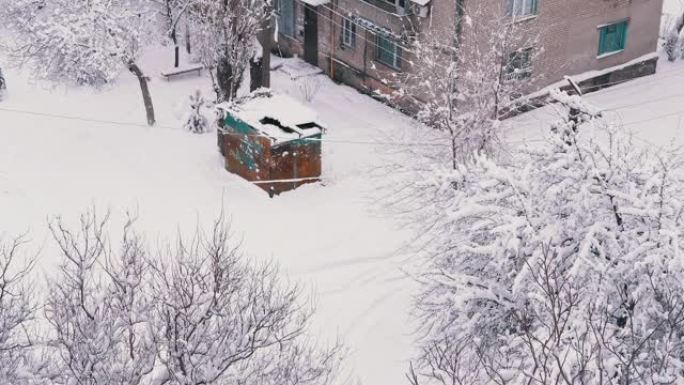 一个生锈的旧车库矗立在一栋住宅砖房的积雪覆盖的院子里