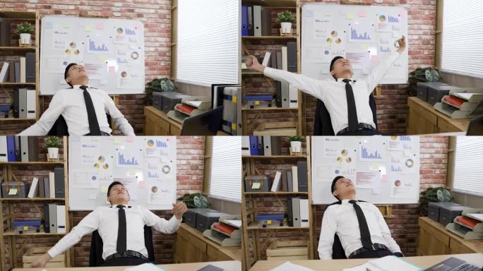 在一间现代化的阁楼办公室里，快乐的亚洲男性经理在电脑上完成工作后，舒服地坐在椅子上伸展身体。