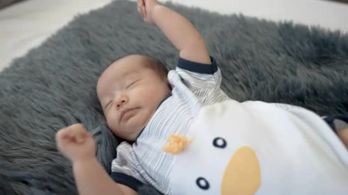 4K 50fps，亚洲两个月大的男婴，在黑色地毯上睡觉和梦游，穿着白色睡衣，家庭健康。