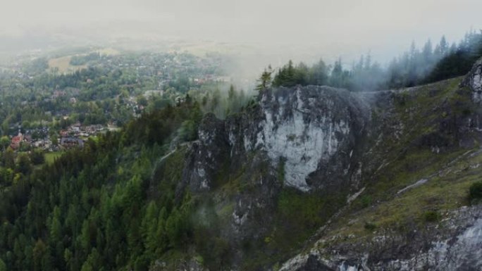 在一片覆盖着云层的岩石悬崖脚下的森林中的一个村庄