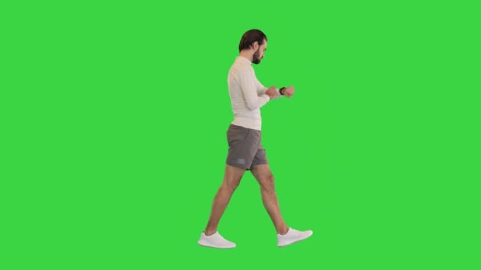 英俊的运动员在绿色屏幕上行走时检查智能手表，色键