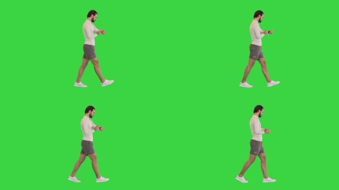 英俊的运动员在绿色屏幕上行走时检查智能手表，色键