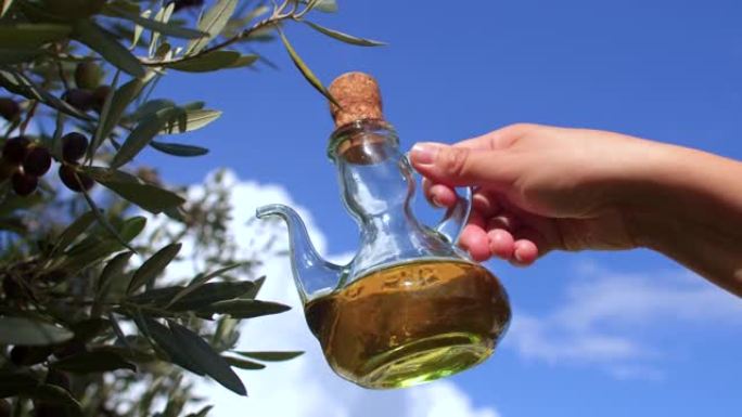 透明的橄榄油容器在农民手中，橄榄树和天空背景。