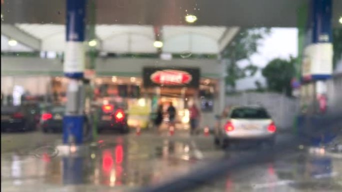 加油站背景模糊，车窗上有雨滴。雨刷移动。
