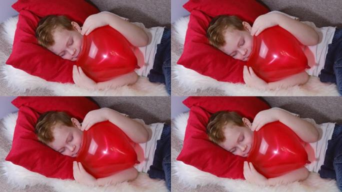 情人节，孩子们。一个可爱的小男孩在情人节做梦，睡觉和微笑，同时拥抱一个红色的心形气球。