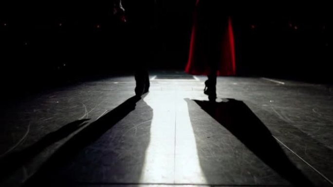 舞厅舞者的脚穿着鞋子和高跟鞋慢慢出现在舞台上。黑暗礼堂前的聚光灯点亮