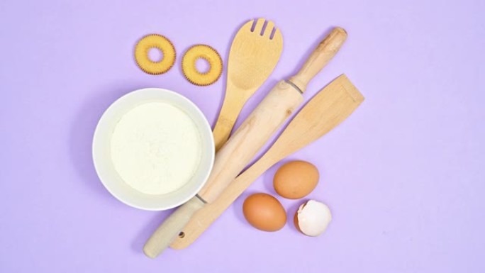木制烘焙厨房工具面粉和鸡蛋以紫色为主题，用于制作饼干。停止运动平铺