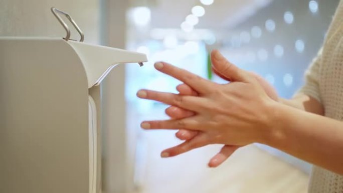特写镜头:女性的手按下液体酒精洗手液的扩散器，将洗手液涂抹在手部