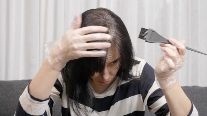 在家染发。中年妇女准备在家染发，看着深色头发重新长出的灰色根部