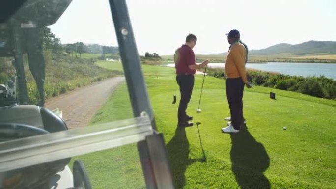 男性高尔夫球手在阳光明媚的高尔夫球场发球盒上聊天