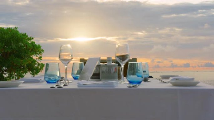 海边的餐桌上有甜食小吃，户外新鲜空气的宴会饮料。白色桌布上装饰有黄色花盘，花瓶上装饰有各种眼镜