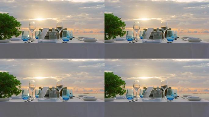 海边的餐桌上有甜食小吃，户外新鲜空气的宴会饮料。白色桌布上装饰有黄色花盘，花瓶上装饰有各种眼镜