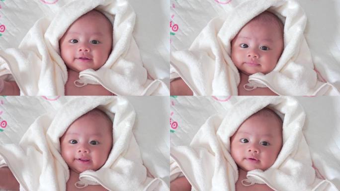 可爱的亚洲新生儿躺在卧室的床上，铺有白色毯子。男婴看着相机，笑着笑脸。小无辜的新生婴儿在生命的第一天