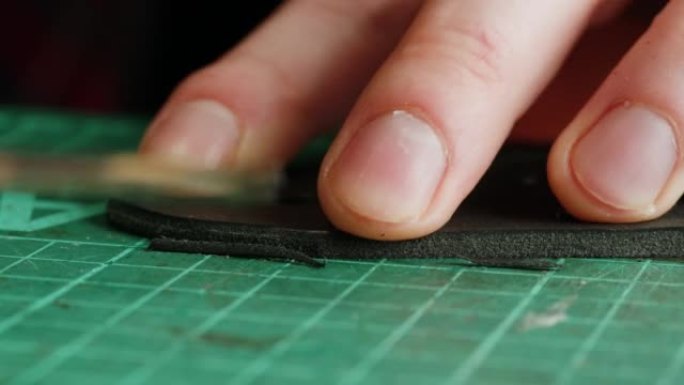 男士裁缝切割人造革特写。工匠在工作场所的桌子上雕刻黑带，制作由真皮动物皮革制成的手工产品。专业工作室