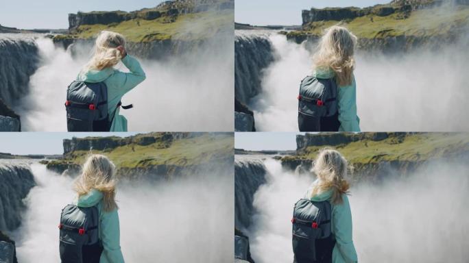 冰岛。金发女人站在悬崖边缘的后部特写，背景是美丽的detifoss瀑布