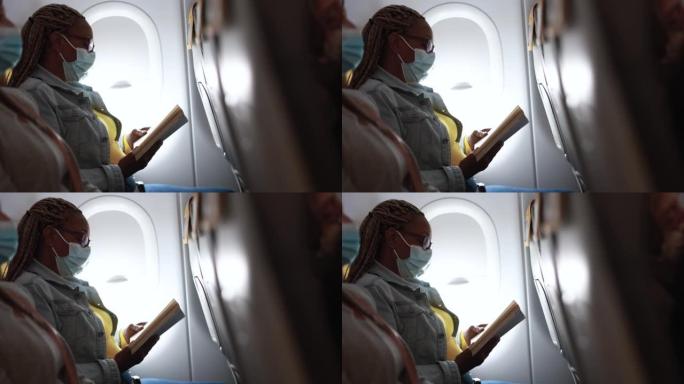 一名非洲成年女性戴着口罩在飞机上看书，以应对新冠肺炎疫情