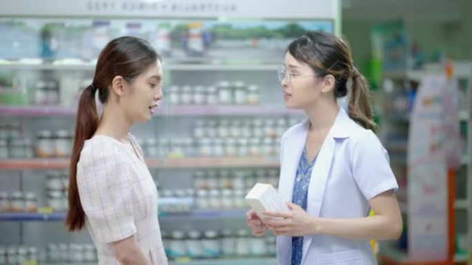亚洲女药剂师根据医生的处方向患者或客户解释药盒上的药物特性，并在客户处向客户提供电子服务付款
