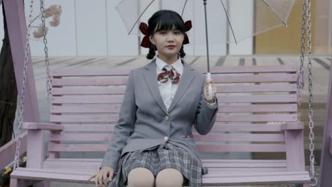 日本女学生穿着校服，坐在吊椅上，手持透明雨伞