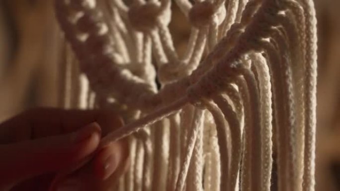 女人的手编织波西米亚风格的花边。女人在棉线上打结以创造花边。创意工作室。现代针织自然装饰理念。绳索工