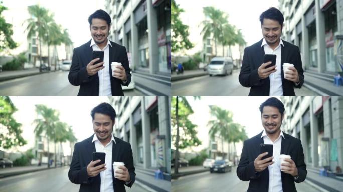 这个英俊的男人正在镇上慢慢散步，微笑着享受着他美味的咖啡。他在智能手机上输入消息并喝热咖啡。我穿着黑
