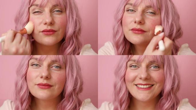 幸福的女人微笑拿着化妆刷，用于在粉红色背景上隔离化妆