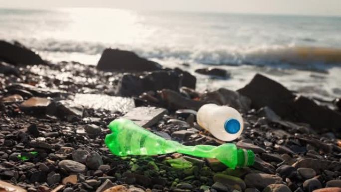 圆石滩上两个肮脏的旧塑料瓶，特写。在背景中，海上冲浪。环境污染的概念
