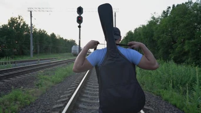 男音乐家沿着铁路铁轨行走，看着离开火车