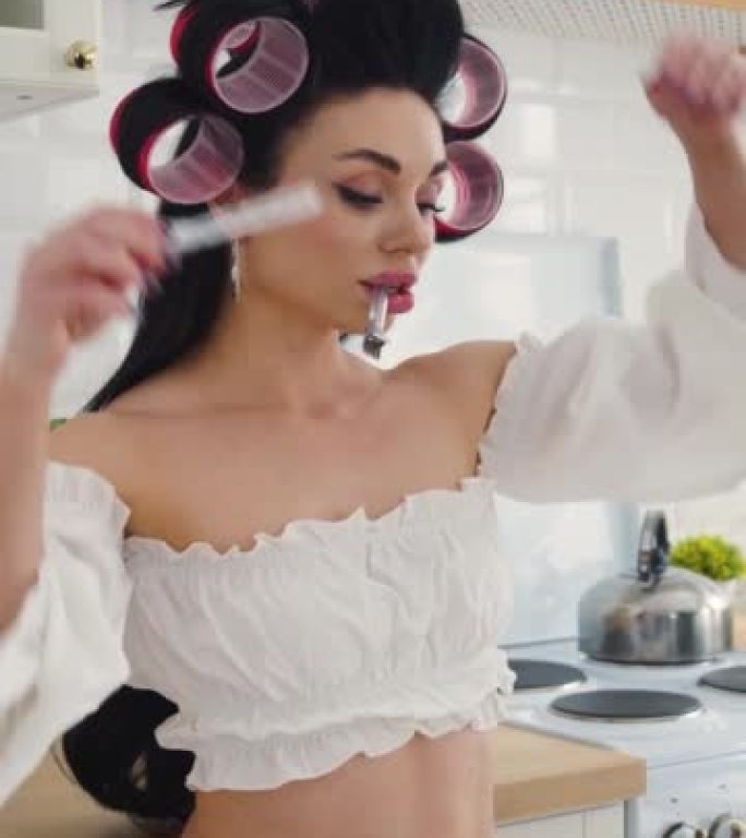 性感的35岁黑发女人在白色内衣站在厨房和插入发夹到她的头发。垂直镜头